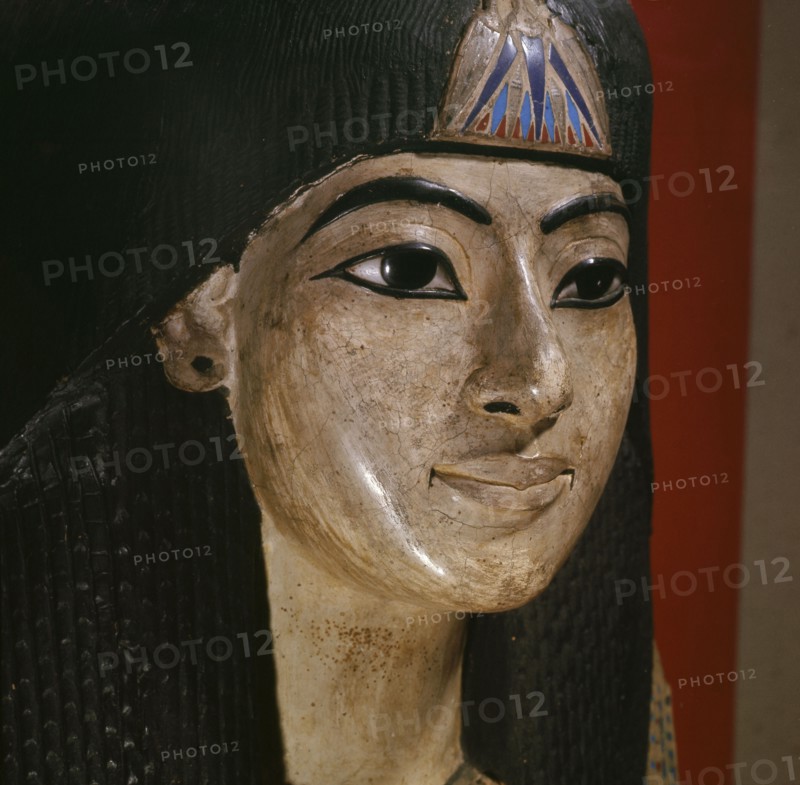 A mummy mask of a man wearing an elaborate collar and a heavy wig adorned with a lotus blossom