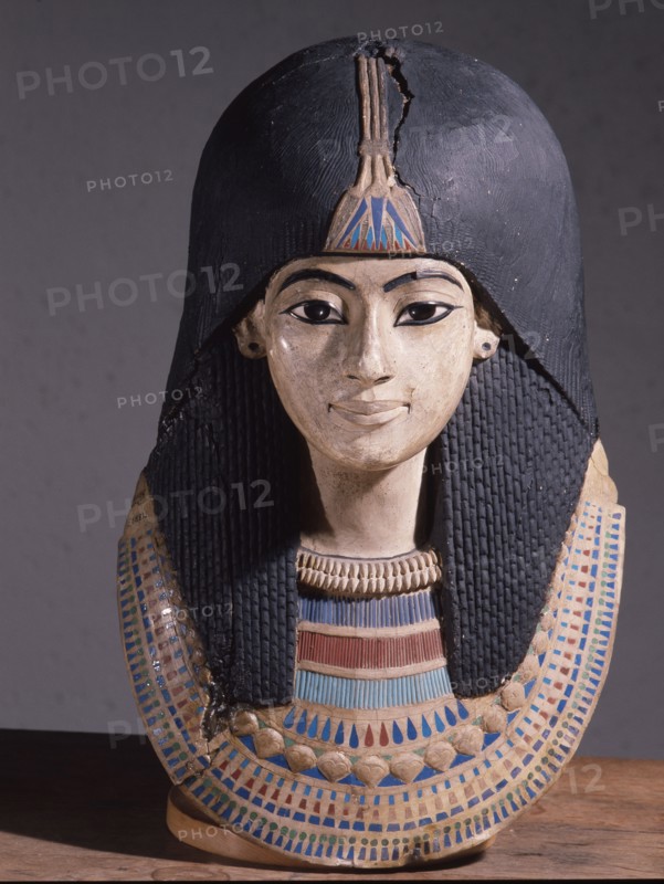 A mummy mask of a man wearing an elaborate collar and a heavy wig adorned with a lotus blossom