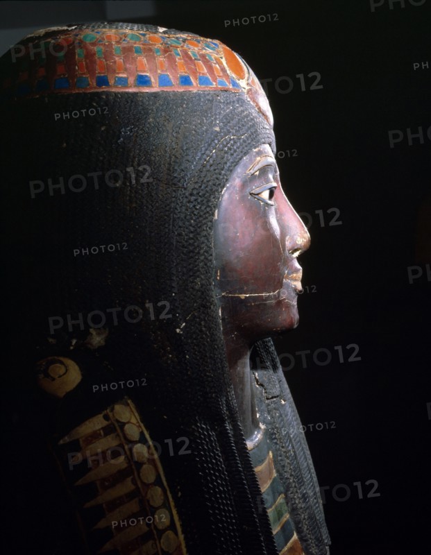 Upper part of an anthropomorphic coffin with blackened face, lotus ornamented wig, chest ornaments, and a picture of the deceased kneeling to offer flowers to Osiris