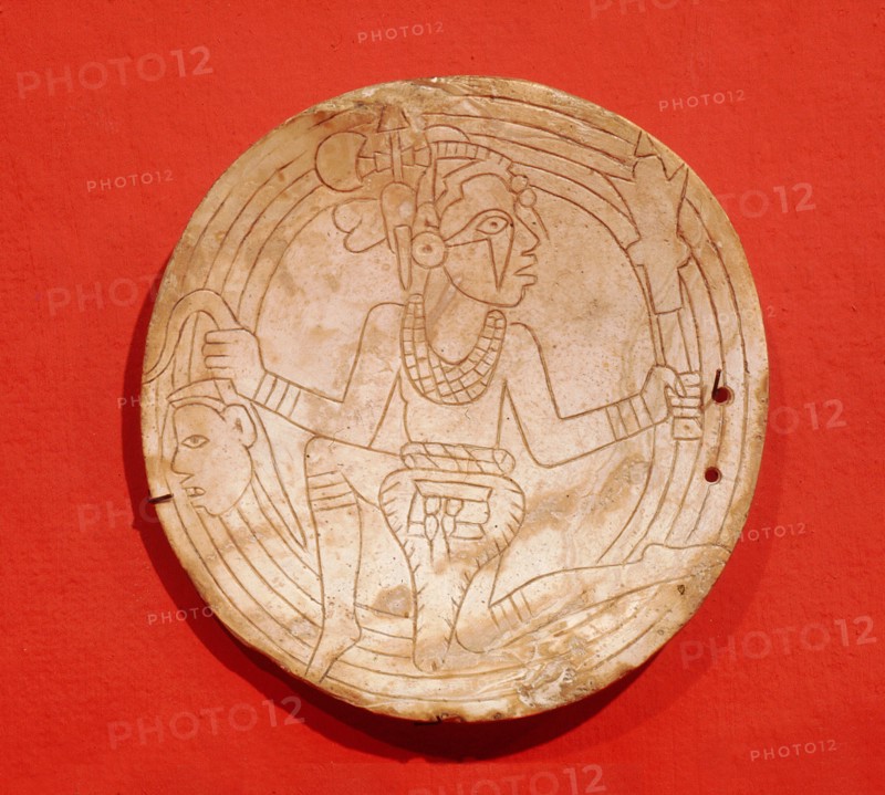 Shell gorget depicting a flying shaman with a deaths head in one hand and a ceremonial mace in the other
