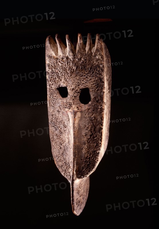 A wooden face mask with remnants of red seeds attached