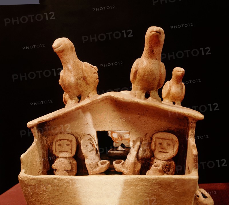 Model of a house with people drinking and birds sitting on the roof