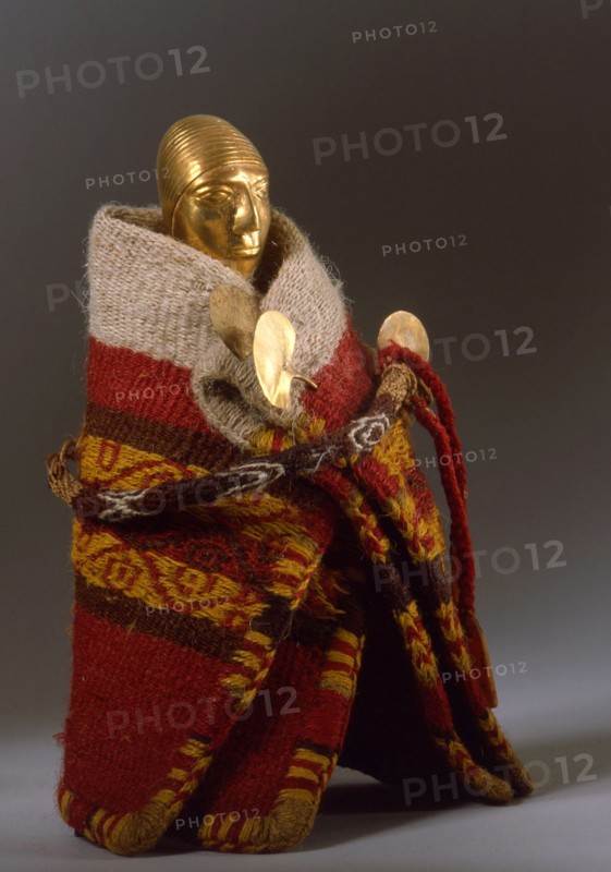 Gold female figurine wrapped in a piece of multicoloured textile fastened with a gold pin