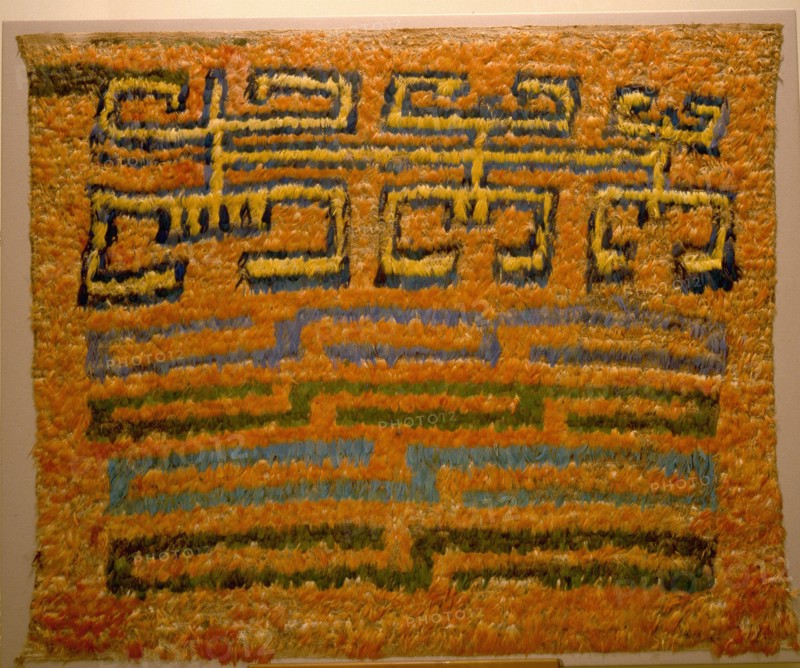 Featherwork tabbard depicting a combination of a tumi knife in the shape of a crescent, two bicephalic dragons and radiant sun faces