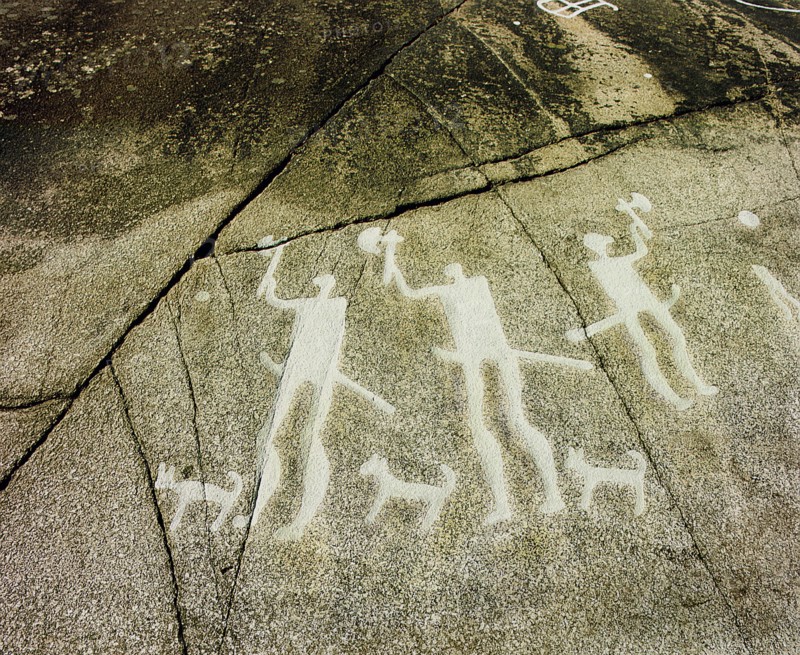 Petroglyph with three men brandishing axes, accompanied by dogs