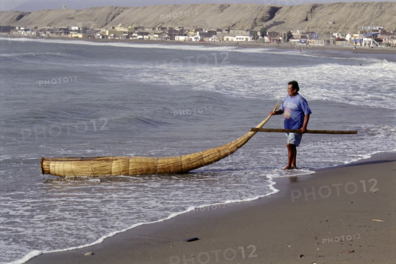 Modern day Moche fisherman guiding a tortora reed boat (caballito) on beach on Peru's northern coast