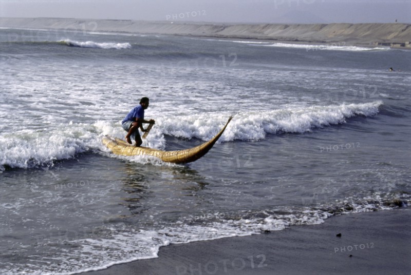 Modern day Moche fisherman guiding a tortora reed boat (caballito) on beach on Peru's northern coast