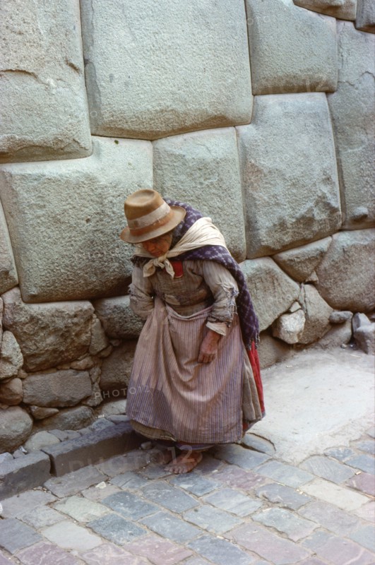 Quechua (Inca) woman in Colonial-period dress walking past typical Inca Masonry in the famous Inca Street of Hatun Rumiyoc, Cuzco