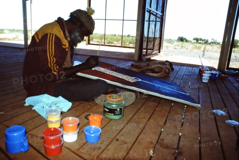 Desert artist Flakky Stevens painting on the verandah at the Warlayirti Culture Centre in the north-west desert region of Western Australia south of Halls Creek