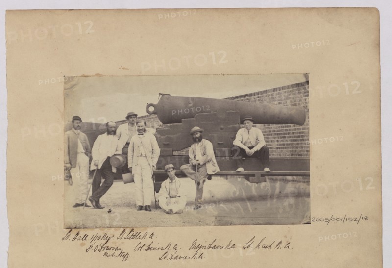 Group of men in civilian clothes pose by cannon