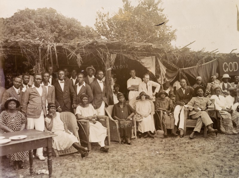 Group standing and seated under palm frond awnings