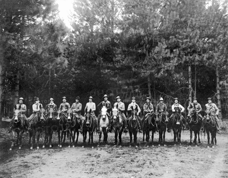 A group of fourteen men on horses pose for a group portrait.