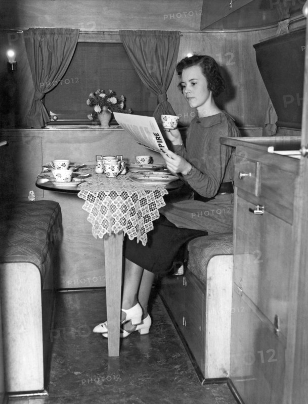 United States:  c. 1936.
A  young woman having breakfast and coffee at a table in a trailer.