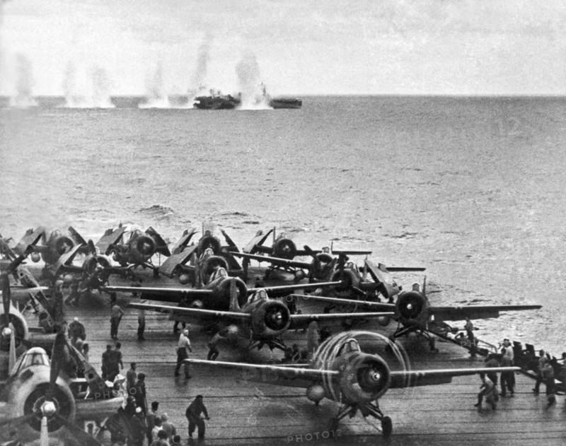 Japanese salvos drop next to the USS White Plains as the USS Kitkun Bay scrambles its fighters during the 2nd Battle of the Philippine Sea.