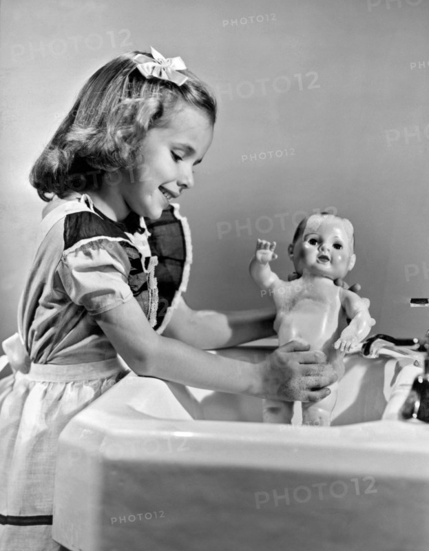 A young girl plays with her new all-vinyl plastic doll that can be washed without fear of damage.