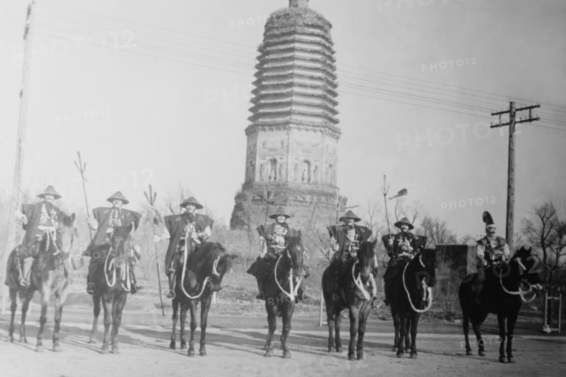 7 Chinese Gendarmes in peaked hats are mounted as skirmishes as cavalry in front of a temple.