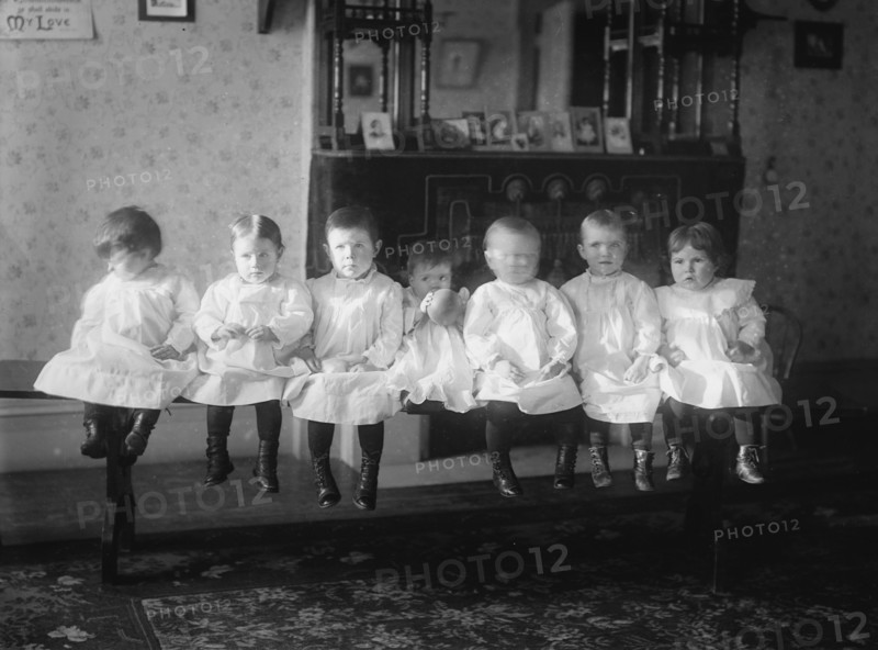 Seven Toddlers in white Dresses seated on Bench 1910