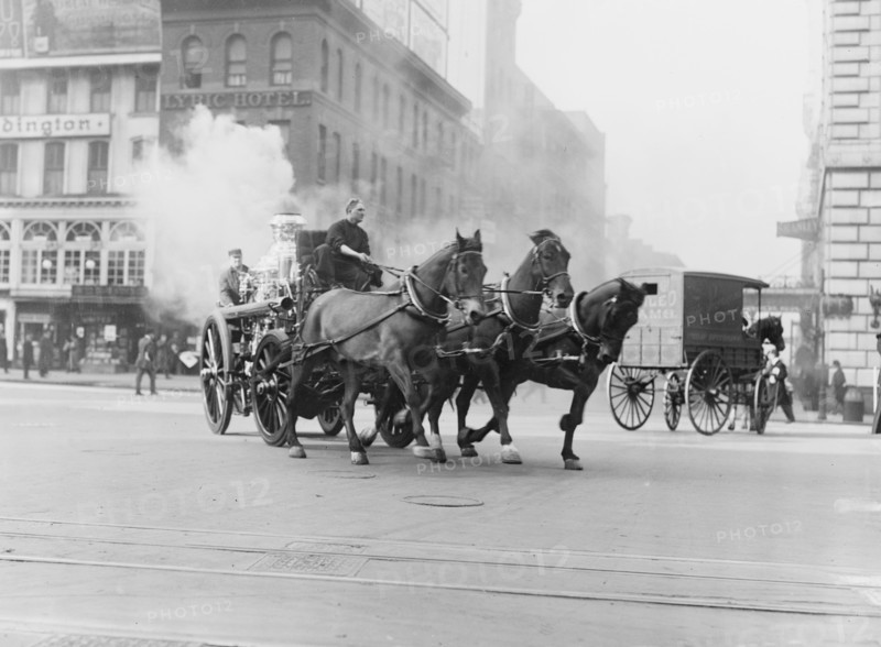 Team of Horses pulls a steam pumper across paved streets toward a fire scene.