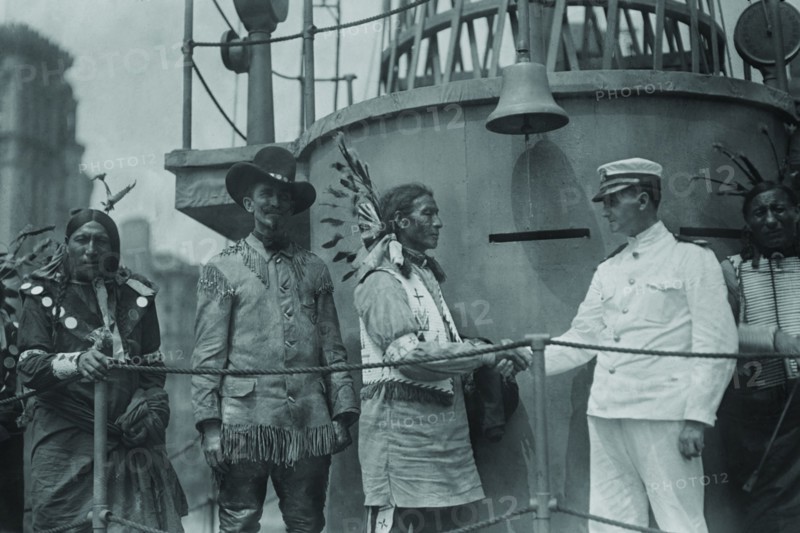 A War Bonneted Native American shakes hands with the Commander of the "Recruit", a facsimile Battleship constructed in the center of Manhattan to aid in enlisting men to fight in Europe in WWI;  1917