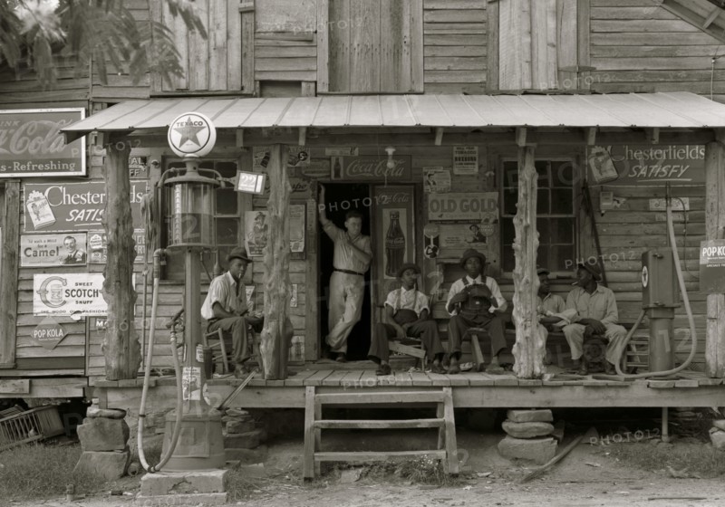 African American and a white store owner on the Porch of a country store 1939