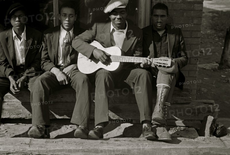 African American on bench while one plays the guitar 1935