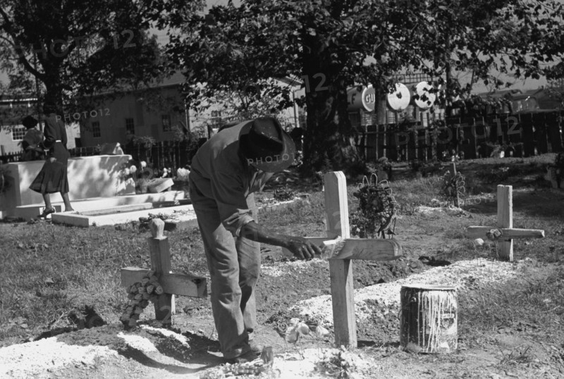 African American paints the crucifix marking a gravesite in a cemetery 1938
