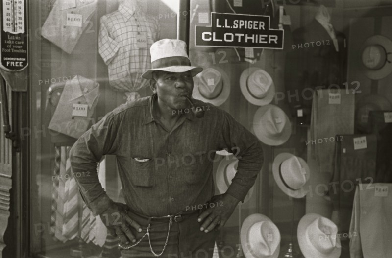 African American Resident of Plain City, Ohio smoking a pipe outside of a clothing store 1935