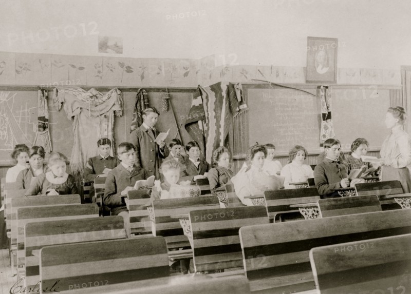 Classroom at the Indian Industrial School, Carlisle, Pennsylvania, showing teacher observing students reading. 1901