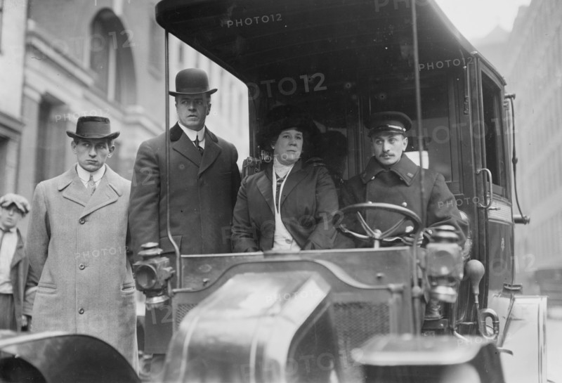 Four dour people, one of whom is their driver look posed while seated in their taxi