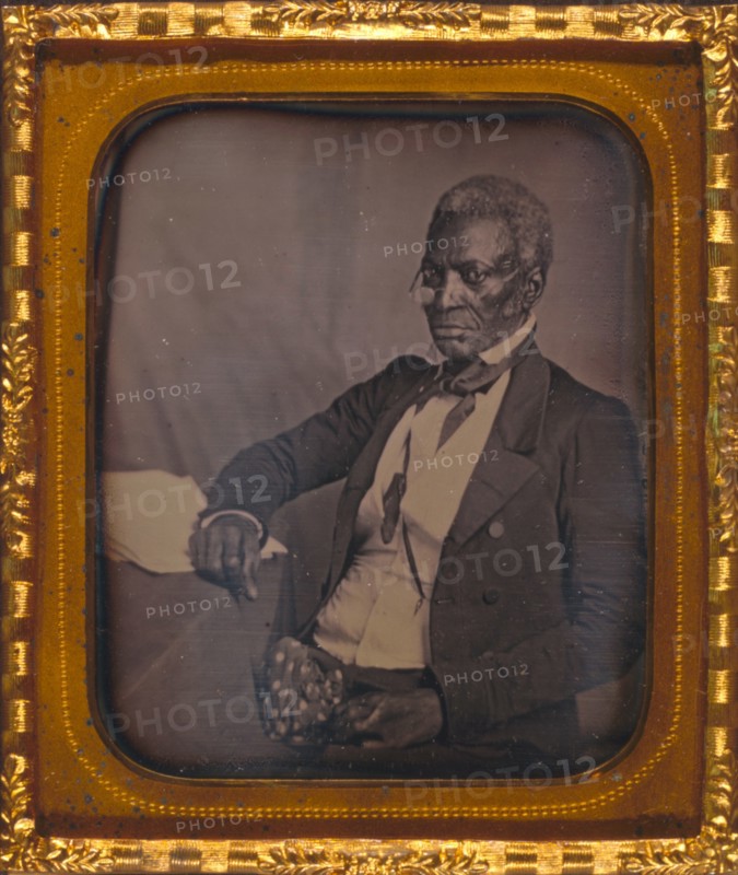 John Hanson, three-quarter length portrait, three-quarters view, wearing glasses, seated at desk 1857