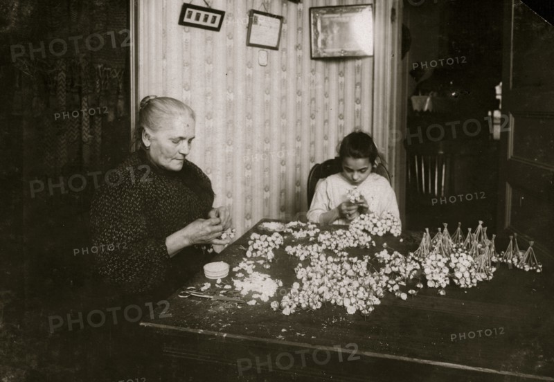 Mrs. Monte Mora, Fifty-five years old, is janitress for a large tenement, 133 W. Houston St., (lives Apt. 7) housing 26 families. When not tending the furnace or occupied with other duties for others and her own family, she makes flowers, assisted by her niece Josephine,  1912