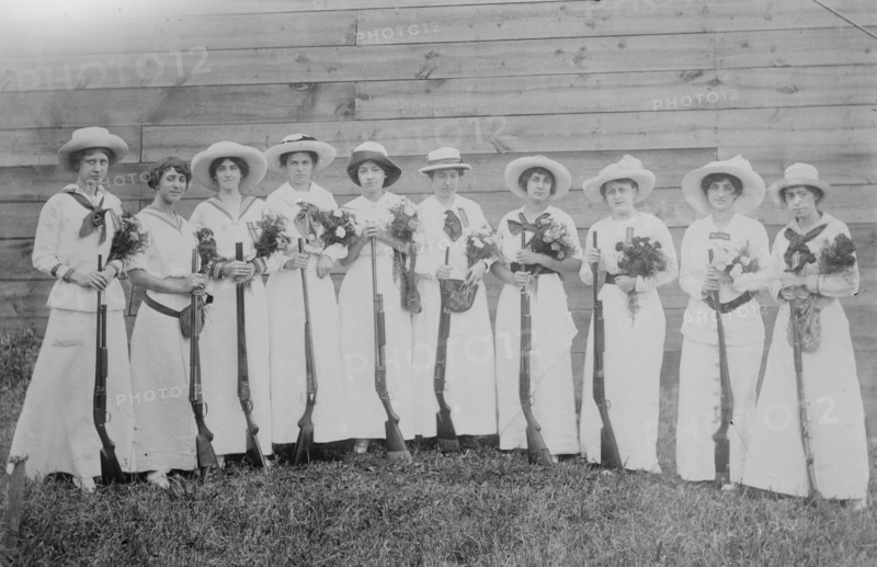 Nemours Women's Trap shooting Club in elegant dress hold both nosegays and rifles.