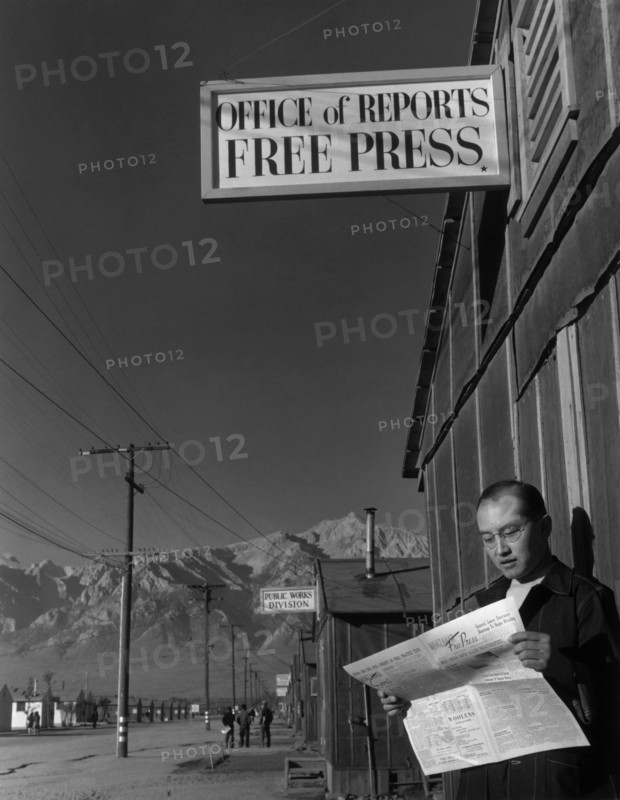 Roy Takeno reading paper in front of office 1943