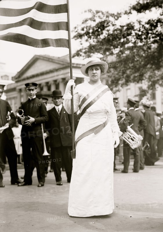 Suffragette holds flag at the head of a waiting male band 1913