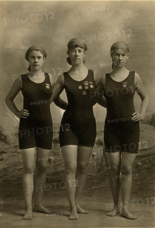 Three young women posing in swimsuits and wearing their swimming competition medals 1920