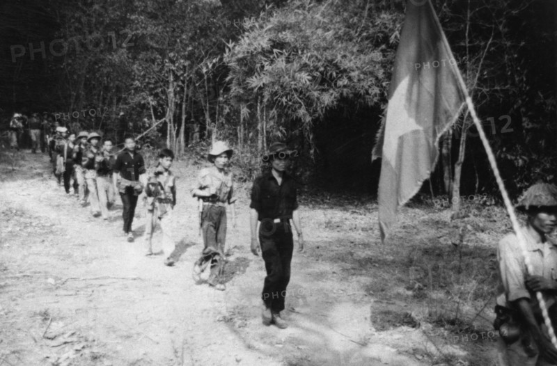 South vietnamese guerrillas file through the jungle along the ho chi minh trail, the flag with a yellow star on a red and blue background is always carried into battle, vietnam war, mid 1960s.