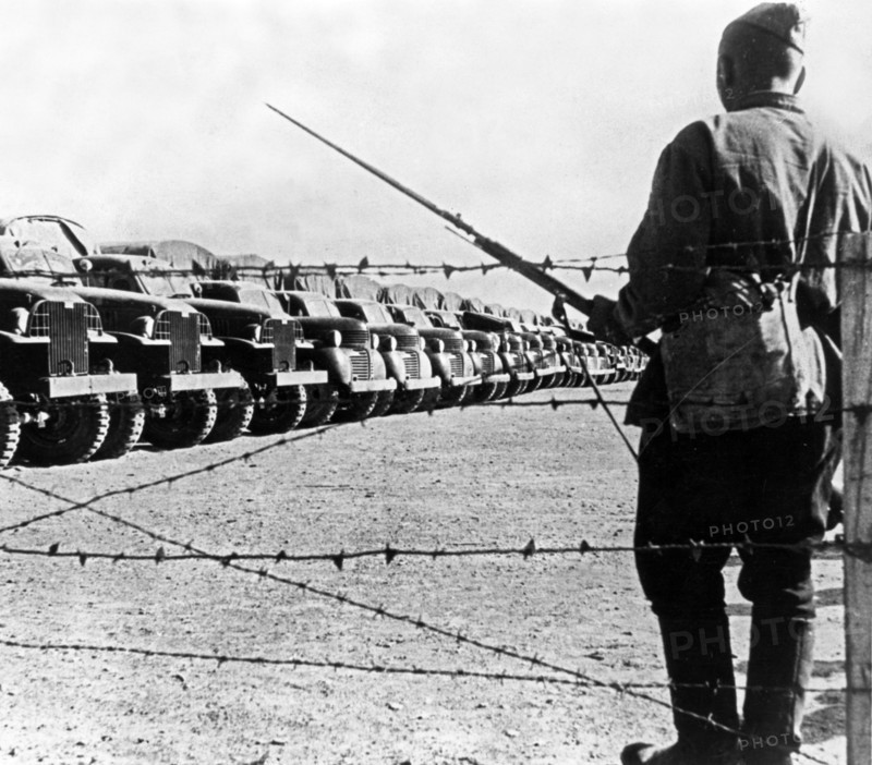 A soldier standing guard over a long line of american trucks at a lend-lease depot in iran, the trucks arrived and were assembled in the persian port and are now awaiting shipment to the soviet union.