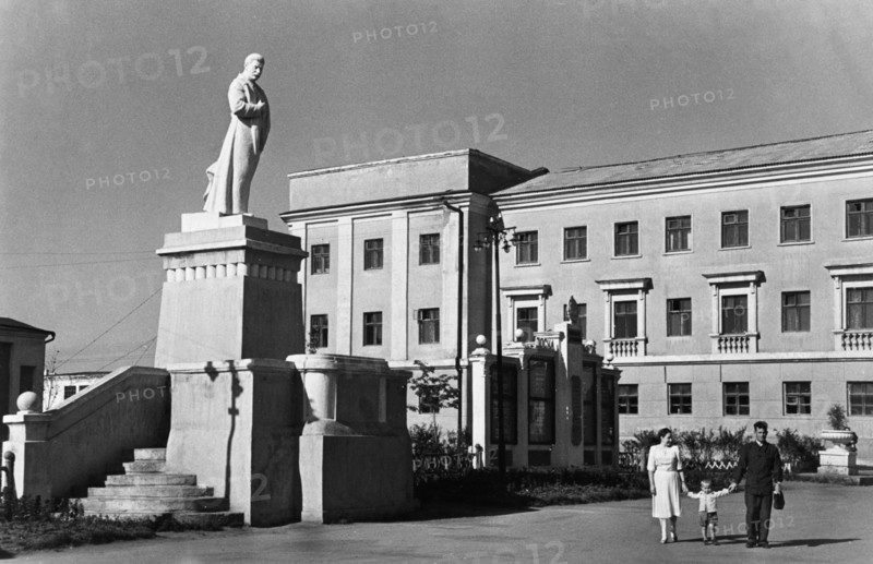 A family strolling under the benificent gaze of a sculpture of josef stalin, 'the great continuer of lenin's cause' on one of the central thoroughfares of stalinogorsk, in the moscow coal basin, ussr, 1950.
