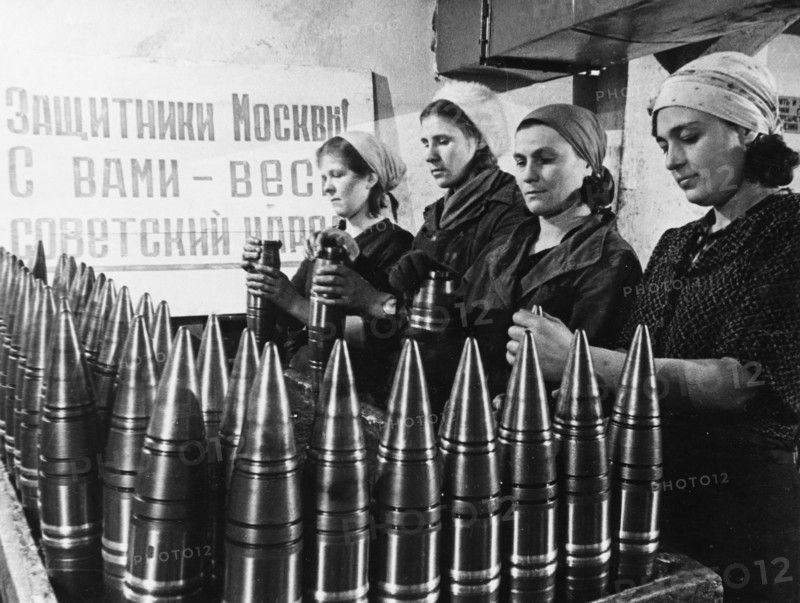 Civilian women making artillery shells at a munitions factory in moscow during world war 2, the sign behind them reads: 'defenders of moscow! the soviet people are with you!'.
