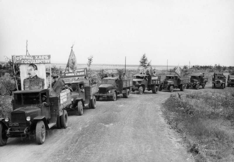 Harvest time on a collective farm in the ussr, august 1947, trucks from the stalin collective farm in the stavropol territory taking grain to the state elevator, the banner reads 'first bread goes to the state'.