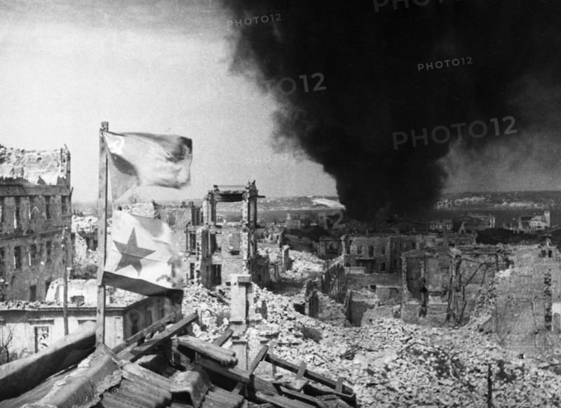 World war 2, siege of sevastopol, soviet flags on the roof of a building occupied by soviet troops in the port of sevastopol, a german tanker is burning in the bay in the background, 1942.