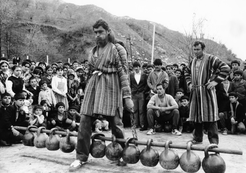 Tajik schoolteacher khamid mirzoev taking part in a weight-lifting contest during a sports festival at the chorbog state farm in the leninsky district of the tajik ssr, these autumn festivals are held to celebrate the end of the cotton harvesting season, 1990.