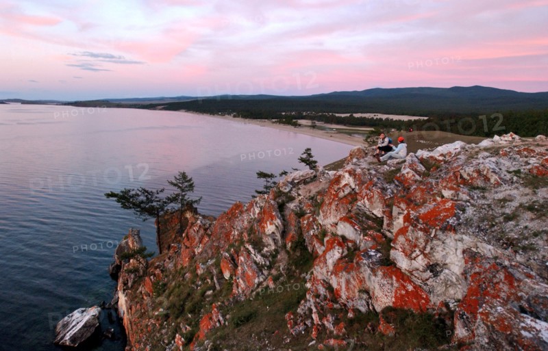 Irkutsk region, russia, september 5, 2006, tourists sit on cliffs on olkhon island, a view of red cliffs on olkhon island and baikal’s saraisky bay.