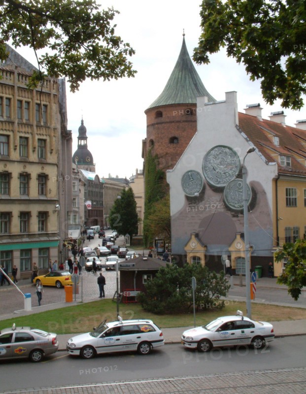Smilsu street, a business area in old riga, latvia, the powder tower (r) and the dom cathedral (in the background), the coins depicted on the right part of the building are lats, the modern latvian currency, in the foreground are riga taxi cabs.