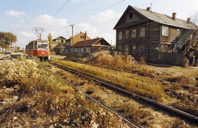 A trolley going past old wooden houses on atypical street in astrakhan, russia.