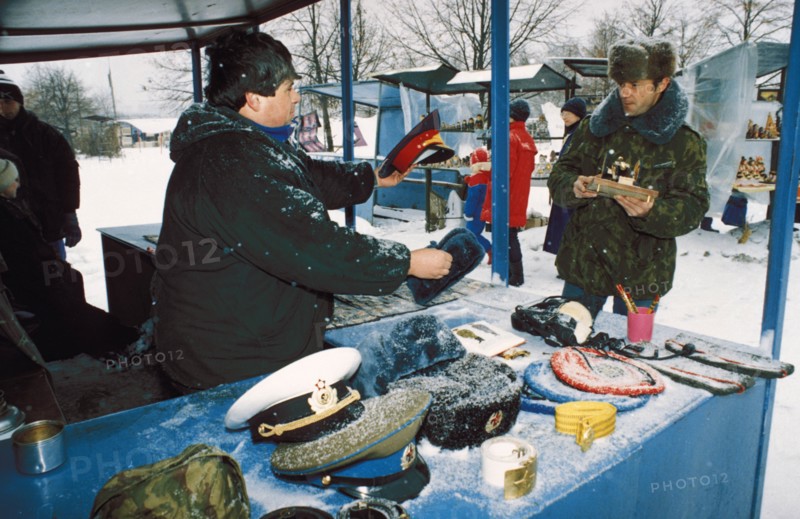 A man selling soviet military hats at the outdoor market (vernissazh) in izmailovo park, moscow, russia where all sorts of things are sold including soviet souvenirs and various arts and crafts, 1990s.