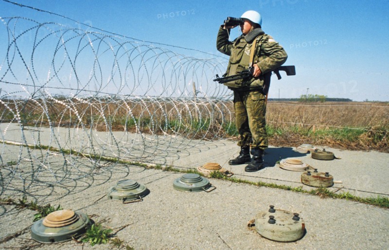 A russian un peacekeeping soldier standing watch on a road barricaded with razor wire and landmines in yugoslavia, april 1994.