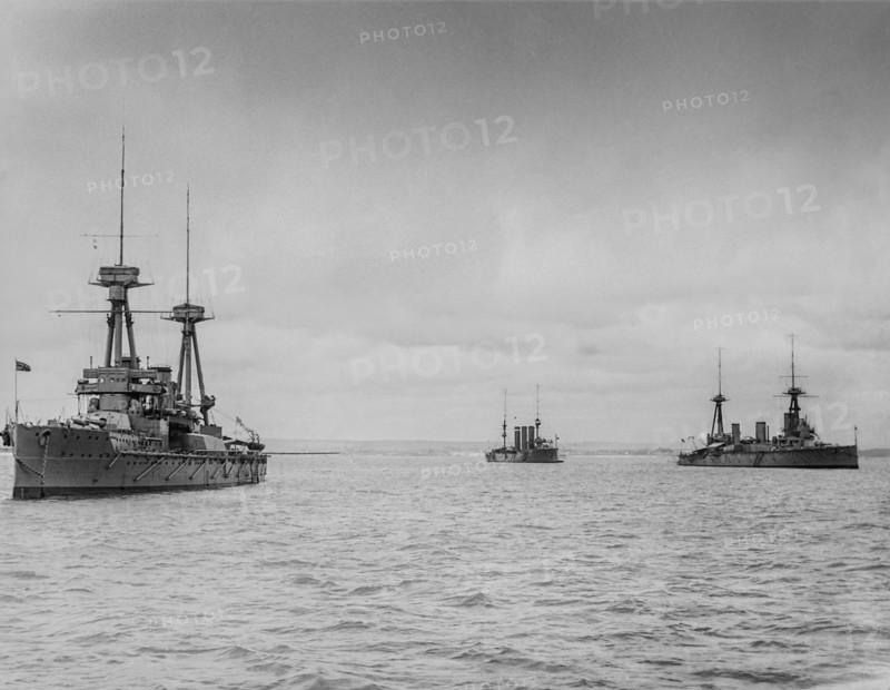 Black and white image of ships moored in the ocean under a cloudy sky