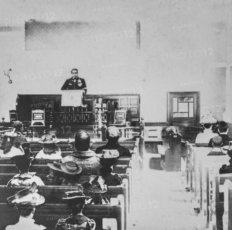 Black and white historic image of a preacher in a pulpit and the congregation in the wooden pews