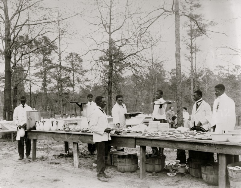 African American men preparing to serve a meal in an outdoor setting among trees